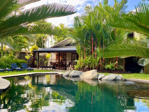 a pool with palm trees in front of a house at Villa Coral - Tropical Oasis Footsteps to Four Mile Beach in Port Douglas