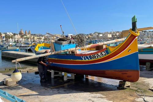 a man standing next to a boat in a harbor at Sunrise Apt - Modern Studio Apt near the Beach in Birżebbuġa