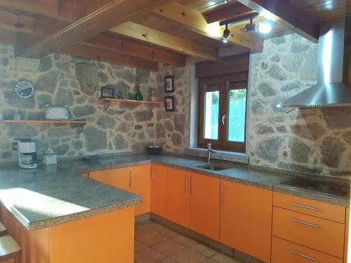 cocina con armarios de color naranja y pared de piedra en Casa Andrés Quilmas, en Carnota