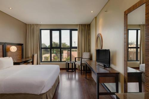 um quarto de hotel com uma cama, uma secretária e uma televisão em Protea Hotel by Marriott Ikeja Select em Ikeja