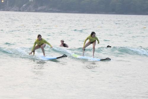 a group of people riding a wave on surfboards in the ocean at Baan Andaman Sea Surf in Patong Beach