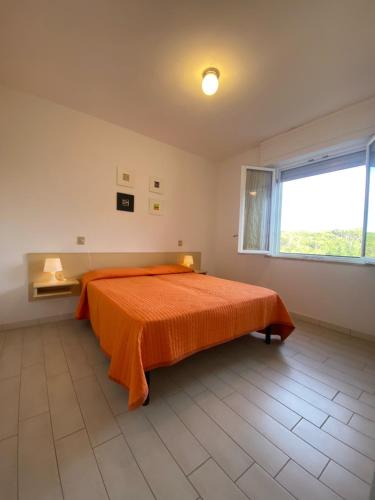 Il Pinolo 2 في مارينا دي سيسينا: غرفة نوم مع سرير مع لحاف برتقالي ونافذة