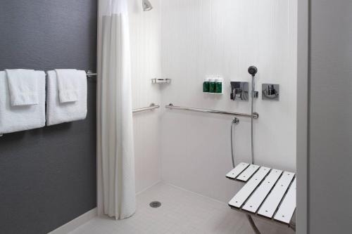 a white bathroom with a shower and a bench at Courtyard by Marriott Raleigh Midtown in Raleigh