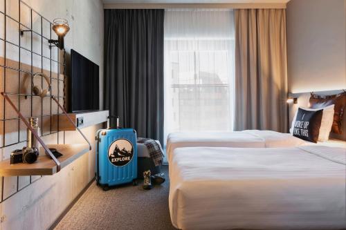 a hotel room with two beds and a blue suitcase at Moxy Munich Ostbahnhof in Munich