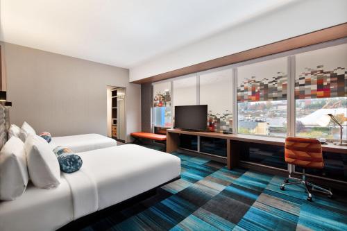 a hotel room with two beds and a desk and a tv at Aloft Seattle Sea-Tac Airport in SeaTac