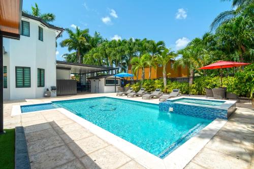 a pool with chairs and umbrellas next to a house at The tropical paradise villa in Miami