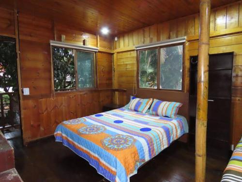 a bed in a room with wooden walls and windows at Cabaña con vista al Río in Ibagué