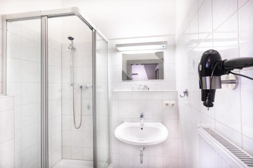 a white bathroom with a sink and a shower at Firzlaff's Hotel in Neumünster