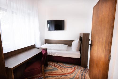 a small room with a bed and a desk with a television at Firzlaff's Hotel in Neumünster