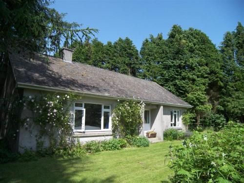 una piccola casa bianca in un cortile alberato di Glenauld Cottage a Kirkcudbright
