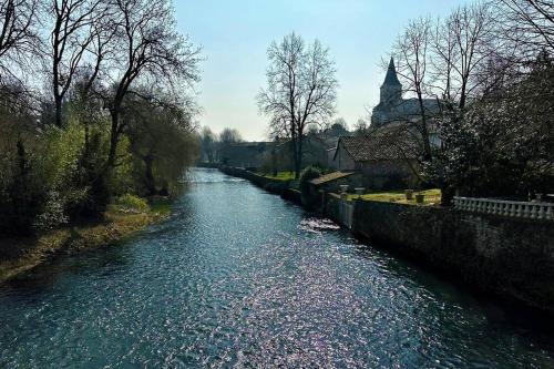 a river with trees and a church in the background at Happiness Verteuil sur Charente in Verteuil-sur-Charente