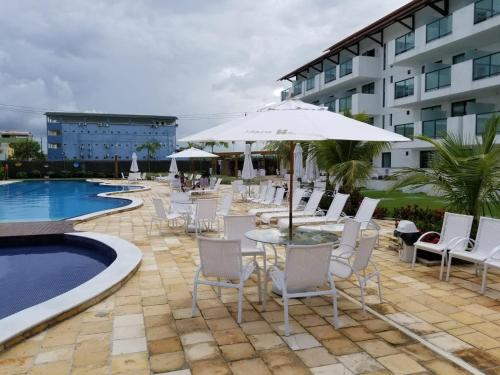 a patio with chairs and an umbrella next to a pool at Laguna Beach Flat in Porto De Galinhas