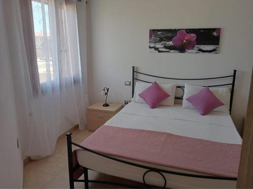 Un dormitorio con una cama con almohadas rosas y una ventana en il Corsaro, en Arbus