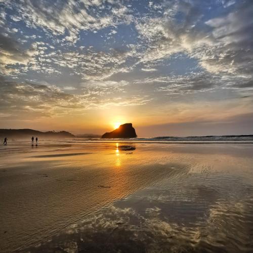 a sunset on a beach with people walking on the sand at Hotel Rural El Texeu in Llanes