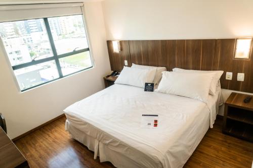a bedroom with a large white bed with a window at Firenze Business Hotel in Palhoça
