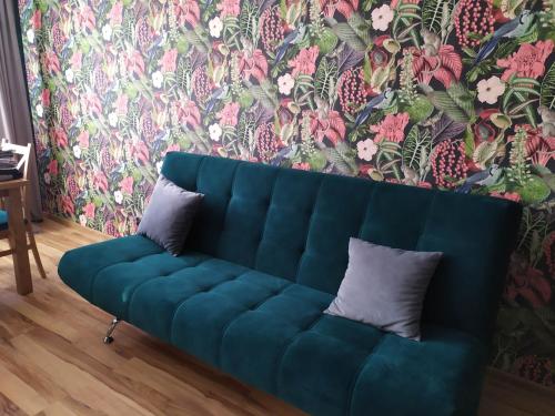 Sofá azul en la sala de estar con papel pintado con motivos florales en Apartament pod Złotą Małpą, en Głuchołazy