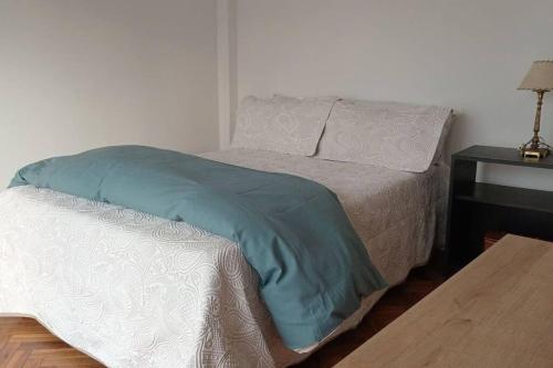 a bed with a blue blanket and a table at Departamento en Recoleta con Balcon Terraza in Buenos Aires