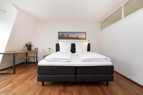 Schlafzimmer mit einem Bett mit weißer Bettwäsche und einem Schreibtisch in der Unterkunft Bike- und Ferienhotel Freiburg in Freiburg im Breisgau