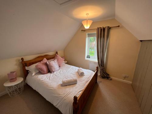 um quarto com uma cama com almofadas cor-de-rosa e uma janela em Holly Farm Cottage em Flixton