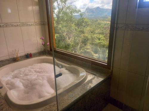a bathroom with a bath tub with a window at Hidromassagem, 5 qtos, 3 stes com vista para a Pedra Azul - Adelta hospedagem in Venda Nova do Imigrante
