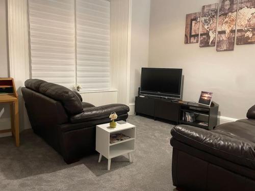 a living room with a leather couch and a television at 5 minutes from Loch Lomond - Newly Renovated Ground Floor 1-Bed Flat in Bonhill