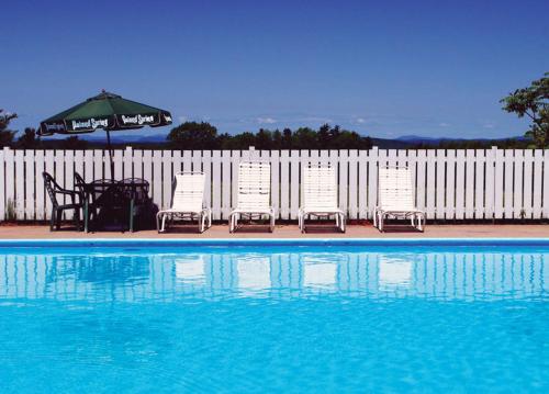 um grupo de cadeiras e um guarda-sol junto a uma piscina em The Presidential Inn at Poland Spring Resort em Poland