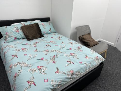 a bed with a blue comforter and a chair at The Grande Residence - Close to Central London & Next to Northfield Tube station in Hanwell