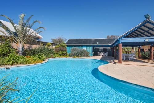 a swimming pool with a patio and a house at Dunsborough Beach Cottages in Dunsborough