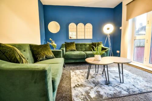 a living room with blue walls and green couches and a table at Dalkeith House By Horizon Stays in Hartlepool