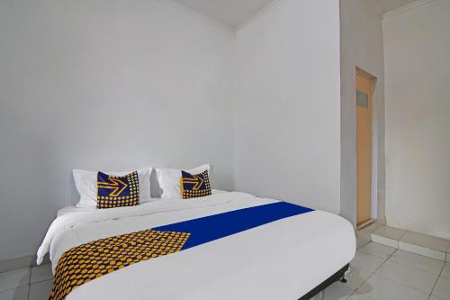 Una cama blanca con almohadas azules y amarillas. en SPOT ON 92498 Fanni Homestay, en Pekanbaru