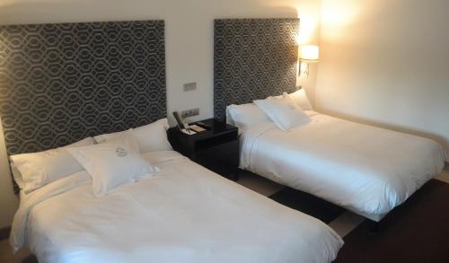 two beds in a hotel room with white sheets at Pazo Los Escudos Hotel Spa & Resort in Vigo