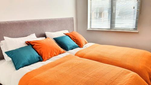 two beds with orange and blue pillows in a bedroom at 11 Putsborough - Luxury Apartment at Byron Woolacombe, only 4 minute walk to Woolacombe Beach! in Woolacombe