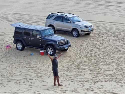 un hombre de pie en una playa con los brazos delante de un jeep en Samuel Dunes, en ‘Izbat Būrīsh al Gharbīyāh
