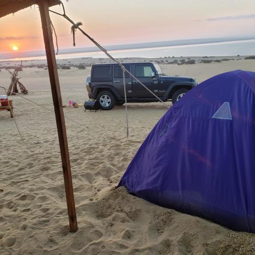 a blue tent and a truck on the beach at Samuel Dunes in ‘Izbat Būrīsh al Gharbīyāh