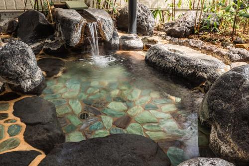 a pool of water with rocks and a waterfall at Atarayo Nishiizu Onsen in Izu