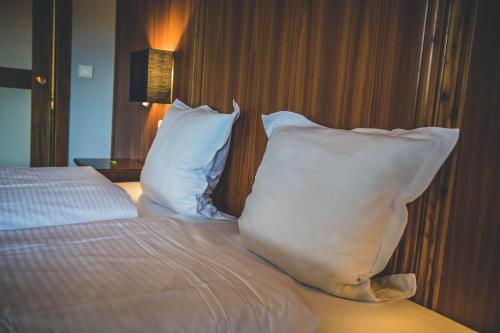 a bed with white pillows and a table with a lamp at Hotel Spa et Restaurant Au Chasseur in Birkenwald