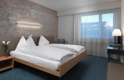 Schlafzimmer mit einem Bett mit weißer Bettwäsche und einem Fenster in der Unterkunft Seeblick Höhenhotel in Emmetten