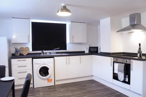 a kitchen with white cabinets and a washer and dryer at Comfy Studio with Transport Links to MCR in Heywood