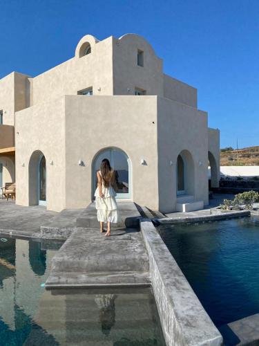 a woman in a white dress standing on a dock near a building at Akrorama private villas and suites in Akrotiri