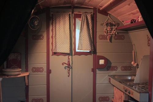 uma cozinha com fogão e uma porta com cortinas em Roulotte irlandaise Polly em Saint-Vincent-en-Bresse