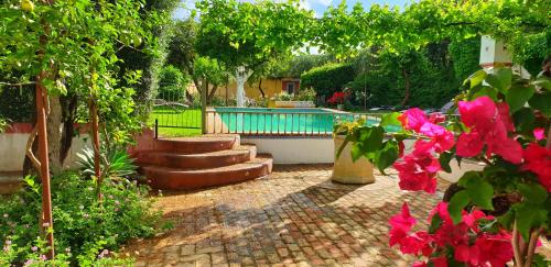 un giardino con piscina e alcuni fiori rosa di Cortijo El Triguero N-398 Ctra Carmona – El Viso del Alcor Km 18 a Carmona