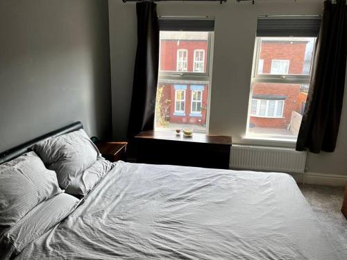a bed in a bedroom with two windows at Stay in the heart of West Kirby in West Kirby