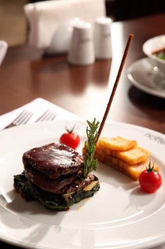 a white plate with steak and bread and tomatoes on a table at Notte Hotel in Ankara