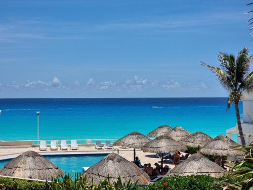 a pool with straw umbrellas and the ocean at Suite Brisas Cancun in Cancún