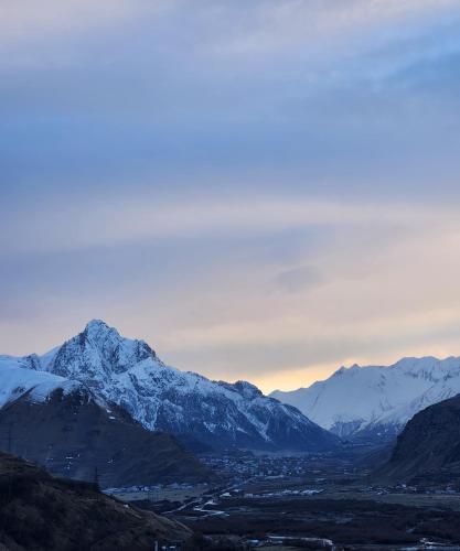 a snow covered mountain range with a town in front of it at Kazbegi Targmani Cottages in Stepantsminda