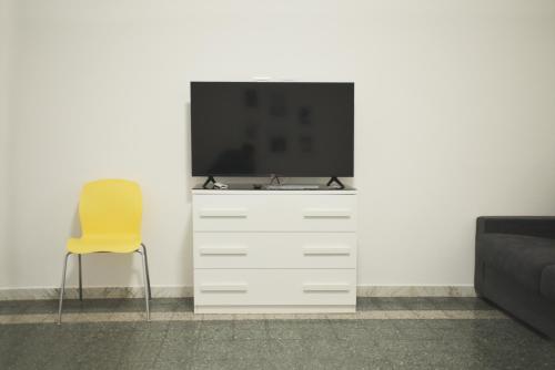 a television on a white dresser with a yellow chair at La Casa di Eva in Brindisi