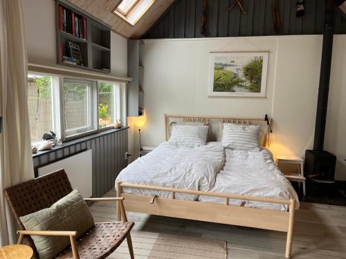 a bedroom with a bed and a chair and windows at Beemster Tiny House in Zuidoostbeemster