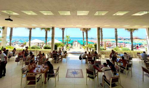 people sitting at tables in a restaurant with a view of the beach at Hotel Vila Lule in Durrës