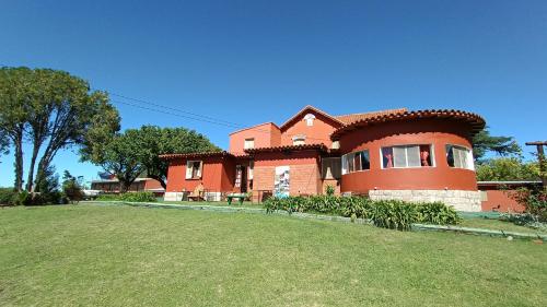 a large red house with a yard in front of it at Castelar - Hotel & Apart in Huerta Grande