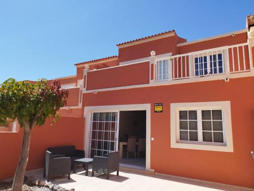 una casa rossa con sedie e un albero di fronte di Spacieux Duplex Casa Maya Caleta de Fuste a Caleta De Fuste